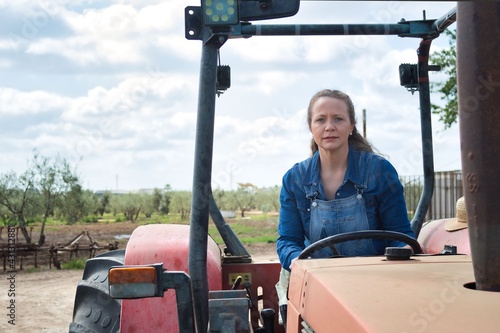 Blonde woman in jeans riding on a red tractor ready to work in the field
