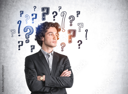 Businessman looking away and background of question marks on grey wall