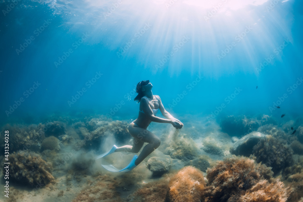 Freediver woman glides underwater with sand in hand. Free diver with fins posing in transparent sea Freediver woman glides underwater with sand in hand. Free diver with fins posing in transparent sea