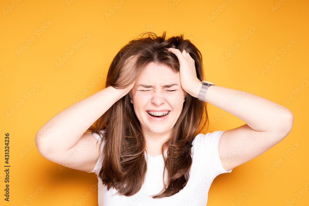 A girl in braces screams from pain in her teeth, touching her hands to her head, closing her eyes A girl in braces screams from pain in her teeth, touching her hands to her head, closing her eyes