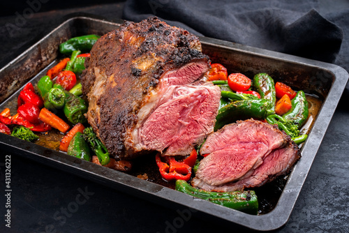 Traditional English barbecue lamb roast with vegetable and gravy sauce offered as close-up in a rustic metal tray