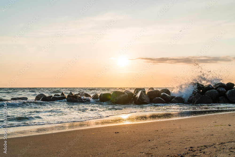wide shot of waves splashing over rocks in sunrise conditions with beautiful beach in the forground