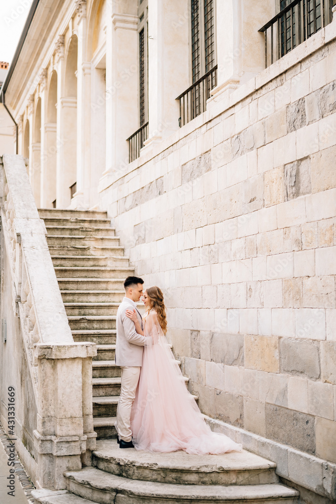 Groom and bride stand on the steps of an ancient building in Bergamo, Italy