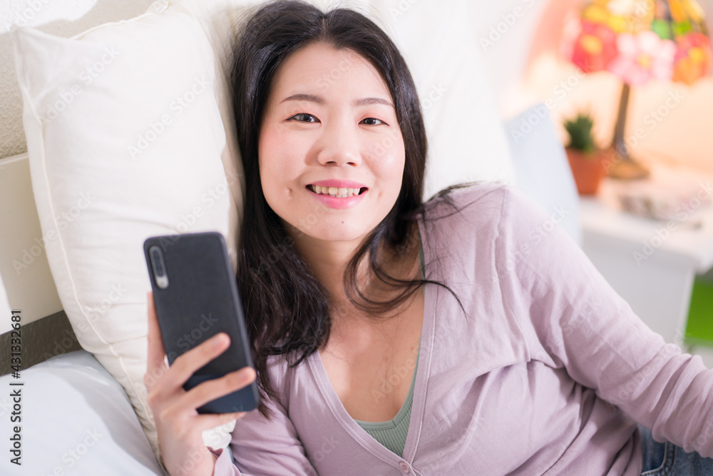 Asian girl with hand phone - home lifestyle portrait of young happy and attractive Chinese woman on bed using internet mobile internet app smiling cheerful in bedroom