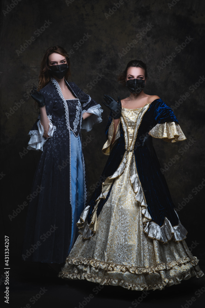 Two women in renaissance dress, face mask and gloves on abstract dark background, coronavirus, covid-19 protection concept