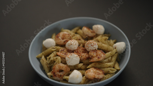 pesto penne with fried shrimps and mozzarella in blue bowl on black background