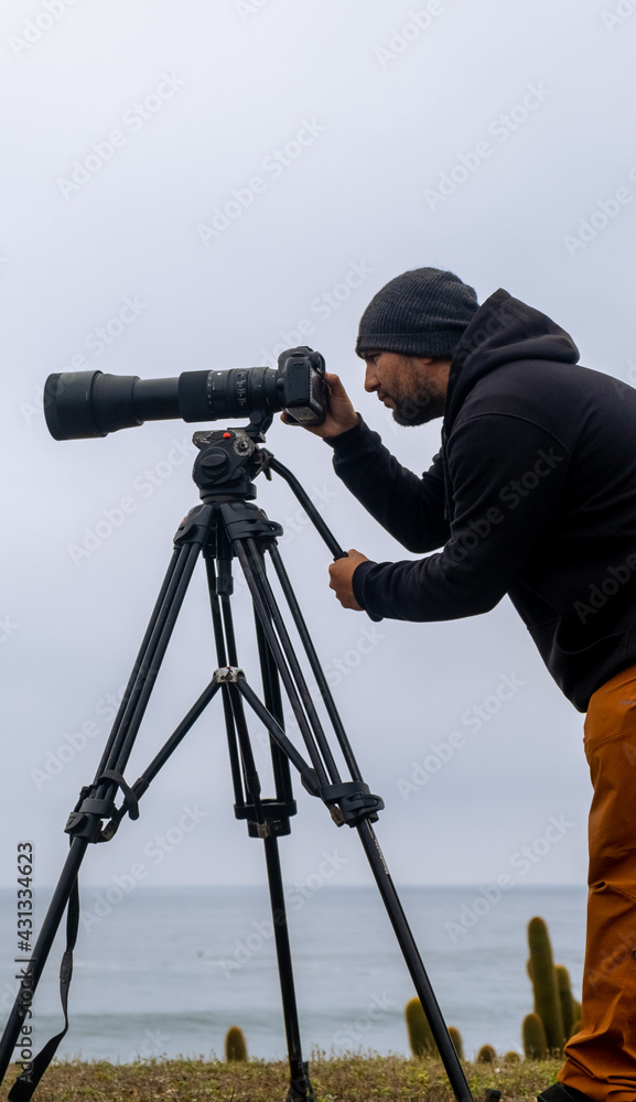 Vertical photo of a nature photographer with his camera and telephoto to take surf photos Chile
