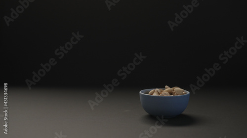 salted large pistachios in blue bowl on black paper background