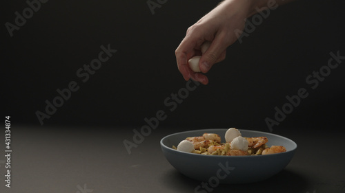 man hand add mozzarella balls to pesto penne with fried shrimps in blue bowl on black background