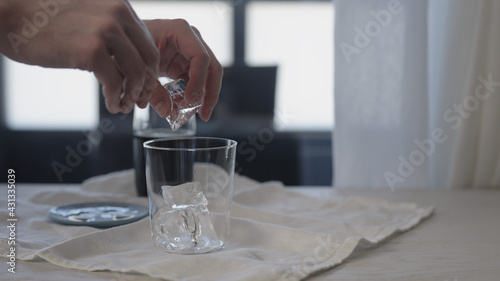 man making cola with ice in tumbler glass on oak table