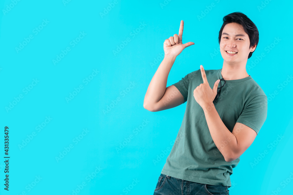 Cheerful Asian male man indicate thumb empty space hand gesture finger point wide smile open mouth wear casual cloth jeans isolated blue color background Cheerful Asian male man indicate thumb empty space hand gesture finger point wide smile open mouth wear casual cloth jeans isolated blue color background