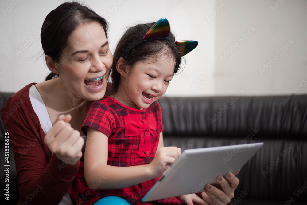 Obraz premium Happy family mother and daughter using digital tablet sitting on sofa online study at home.