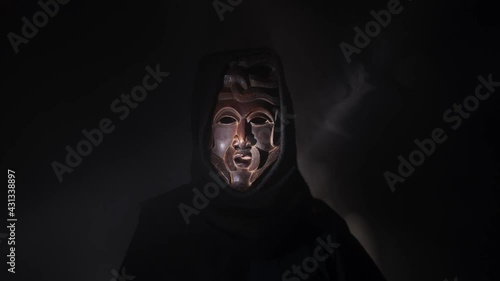 Creepy, masked cultist standing in a dark room. Scary horror scene, mysterious man in a tribal mask isolated on a black background. Eerie mask, devil concept.