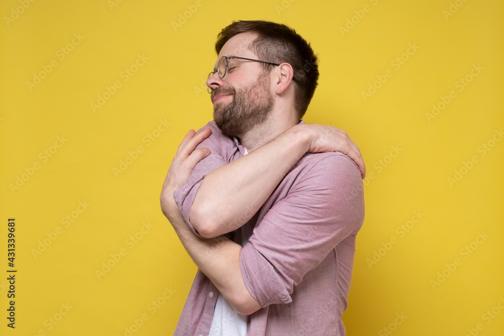 Funny bearded man in round glasses hugs himself, he suffers from narcissism or dreams of love, closes eyes and smiles cute. Funny bearded man in round glasses hugs himself, he suffers from narcissism or dreams of love, closes eyes and smiles cute.