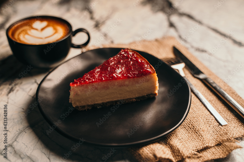 Fototapeta premium Strawberry cheesecake served on a black plate with coffee latte
