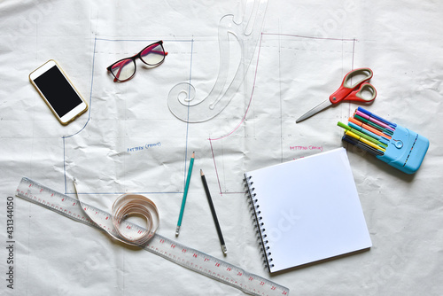 Sewing supplies on a draft paper of pants, sewing thread, scissors, , colorful pen, pencil, ruler, sketch book, smartphone ,centimeter tape and equipment