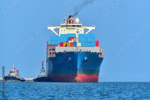 A modern blue container ship moving in calm water, Cargo ship bulbous bow view Cargo ship with tug boat in sea freight, Shipping.