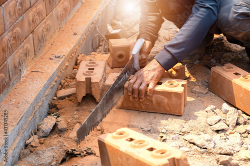 Construction workers sawing red bricks with hand saw at construction site. construction, Building manual work photo