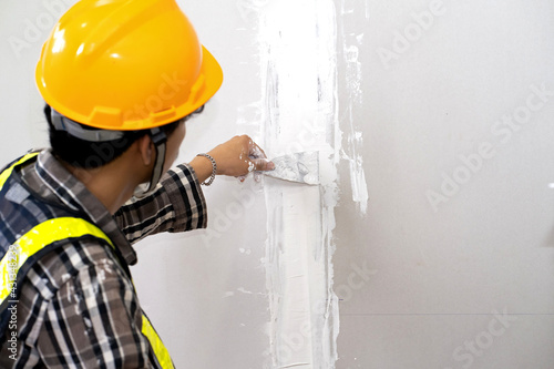 Construction worker plastering gypsum board or plasterboard panels wall with trowel. Home interior drywall works, renovation or construction