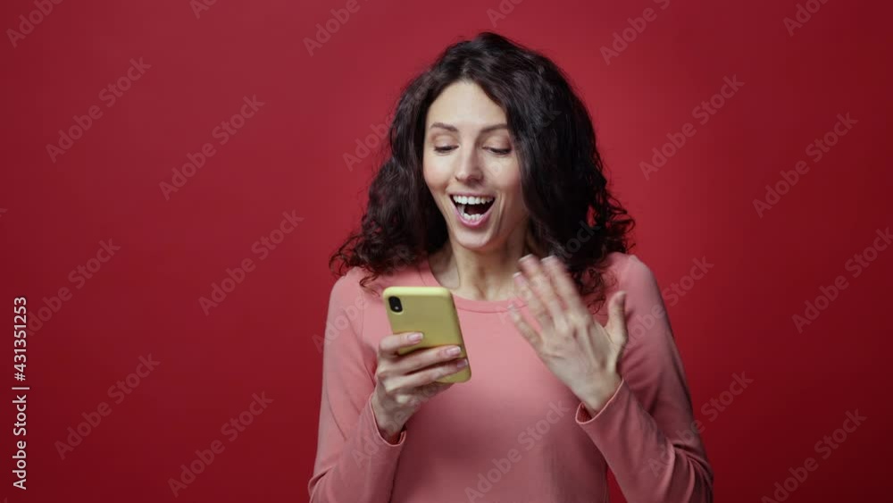 Studio shot of shocked millennial woman reading email, sms or message on smartphone scream wow with excitement and surprise expression on happy smiling face. Overjoyed excited female on red background Studio shot of shocked millennial woman reading email, sms or message on smartphone scream wow with excitement and surprise expression on happy smiling face. Overjoyed excited female on red background