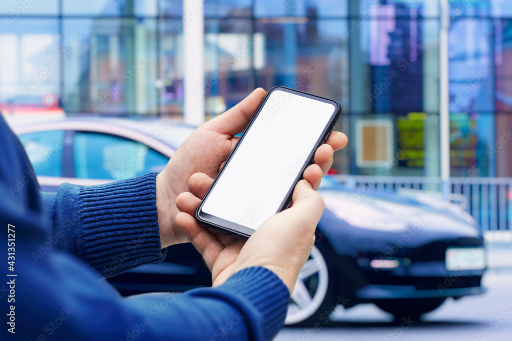 Man holds a smartphone in his hands. Mock up phone with white screen on the background of the car. Man holds a smartphone in his hands. Mock up phone with white screen on the background of the car.