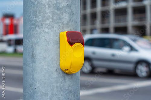 Yellow button at a traffic light for pedestrians on the background of a road with cars.