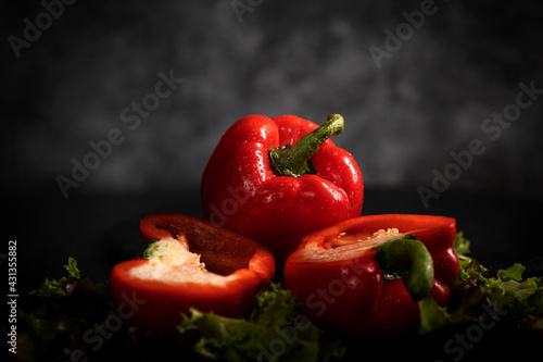 Rote Paprika liegt auf den Salatblättern, auf dem schwarzen Hintergrund. Eine Paprika ist durchgeschnitten, die zweite ist im Stück.Querformat