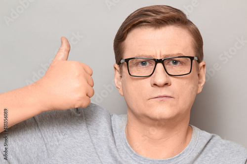 Portrait of serious man raising thumb up in approval gesture