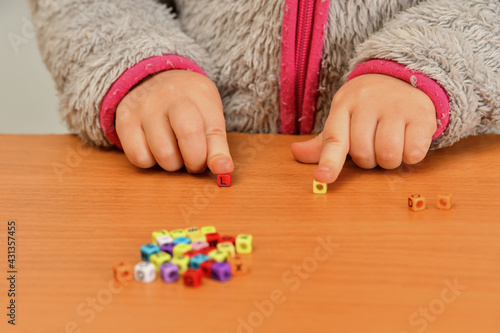 A small child plays with colored letters and tries to put them into words. Preschool education concept.