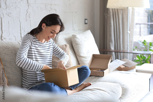 Beautiful young woman is holding cardboard box and unpacking it sitting on sofa at home. photo