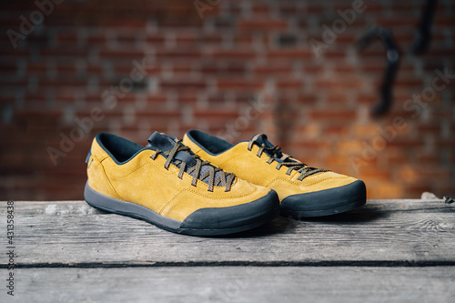 A product shot of outdoor shoes. Low approach hiking boots on wooden ground with a brick wall in the background. 