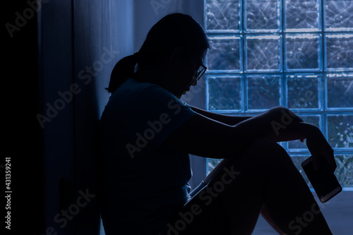 Silhouette depress woman sitting and hold smartphone in hand.