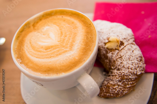Cup of tasty cappuccino with heart and croissant on a side