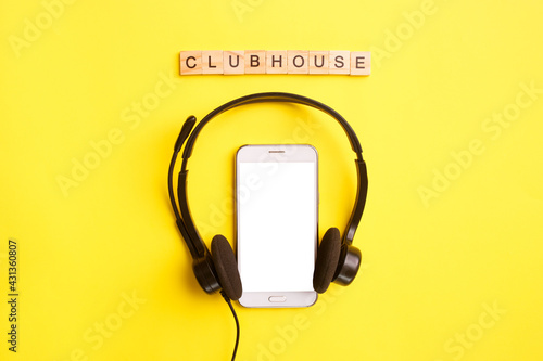 Headphones and smartphone with wooden letters on a yellow background. Clubhouse social media concept. Mock up, copy space, flat lay, top view photo