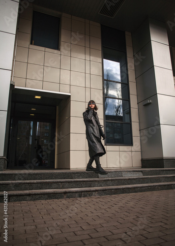 Woman in black leather coat and glasses walks in hurry from building of business center