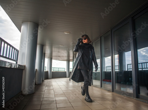 Woman in black leather coat and glasses walks in hurry from building of business center © okostia
