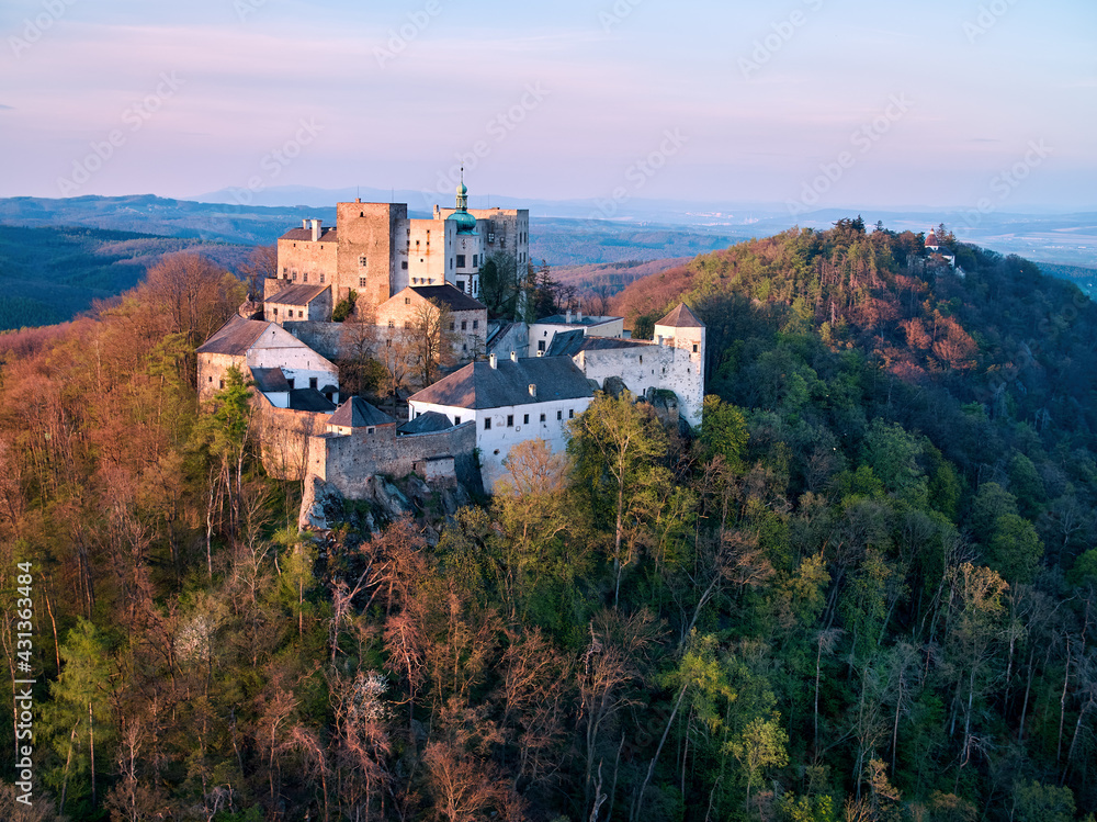 Buchlov Castle. Aerial view on monumental castle in Romanesque Gothic style, standing on a wooded hill against Saint Barbara’s Chapel on the hill in background. Spring, tourism hot spot. Czech castles