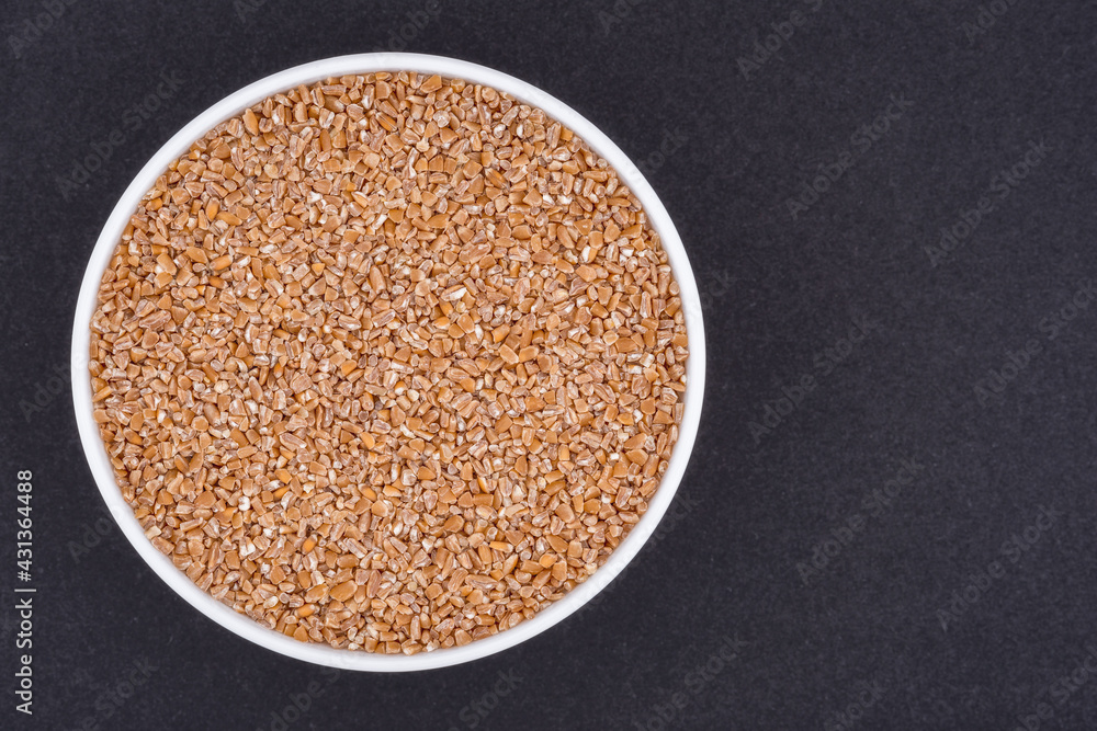 White glass bowl of wheat groats. Isolated on a dark grey background. Top view close up White glass bowl of wheat groats. Isolated on a dark grey background. Top view close up
