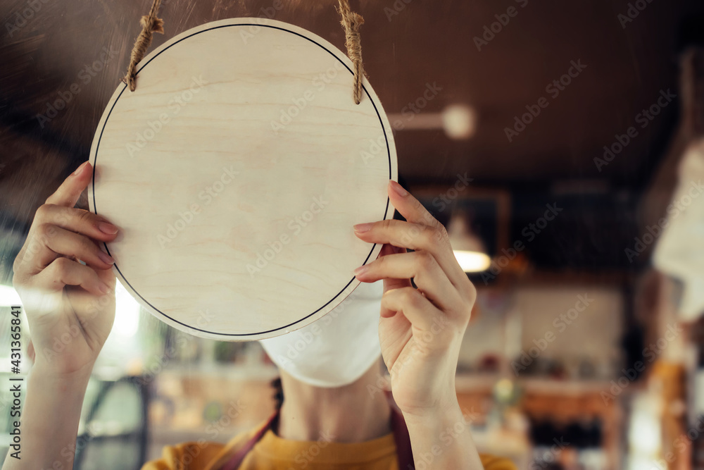 waitress staff wearing protection face mask turning blank vintage wooden sign board hanging on glass door in cafe restaurant, advertising, advertisement marketing and small business owner concept