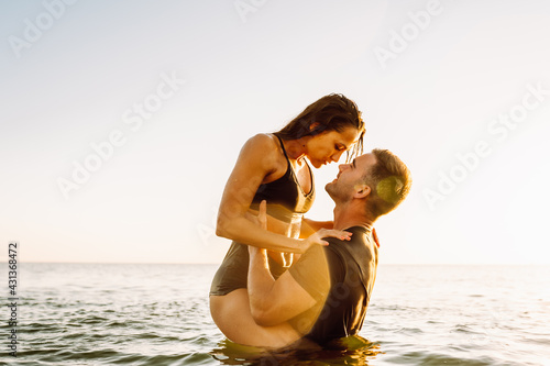 Happy young fit couple embrace each other with love in the sea or ocean at summer sunset. Romantic mood, tenderness, relationship, vacation concept. photo