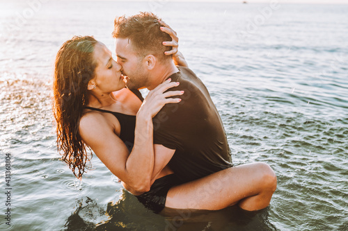 Tableau sur toile Happy young fit couple embrace each other with love in the sea or ocean at summer sunset