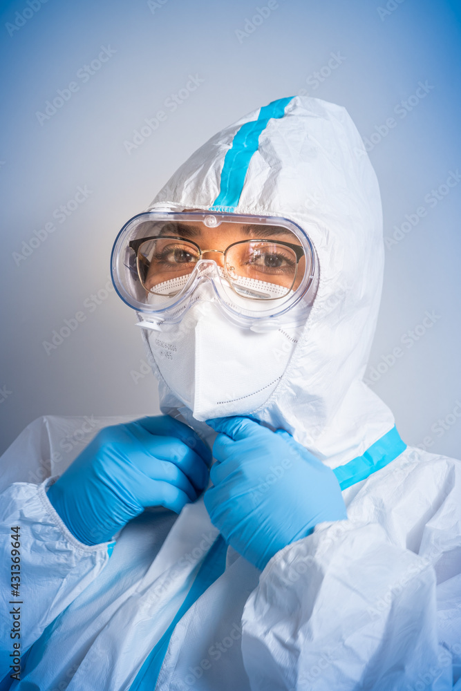 Portrait of female nurse scientist wearing white ppe suit, medical protective scrabs glasses, shield and face mask with blue gloves. Coronavirus pandemic covid-19. Vaccination in medical clinic. Portrait of female nurse scientist wearing white ppe suit, medical protective scrabs glasses, shield and face mask with blue gloves. Coronavirus pandemic covid-19. Vaccination in medical clinic.