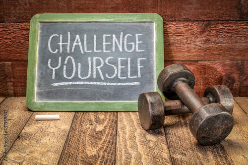 Fototapeta Naklejka Na Ścianę i Meble -  challenge yourself motivational concept, white chalk writing on a slate blackboard with a pair of vintage dumbbells, fitness and personal development