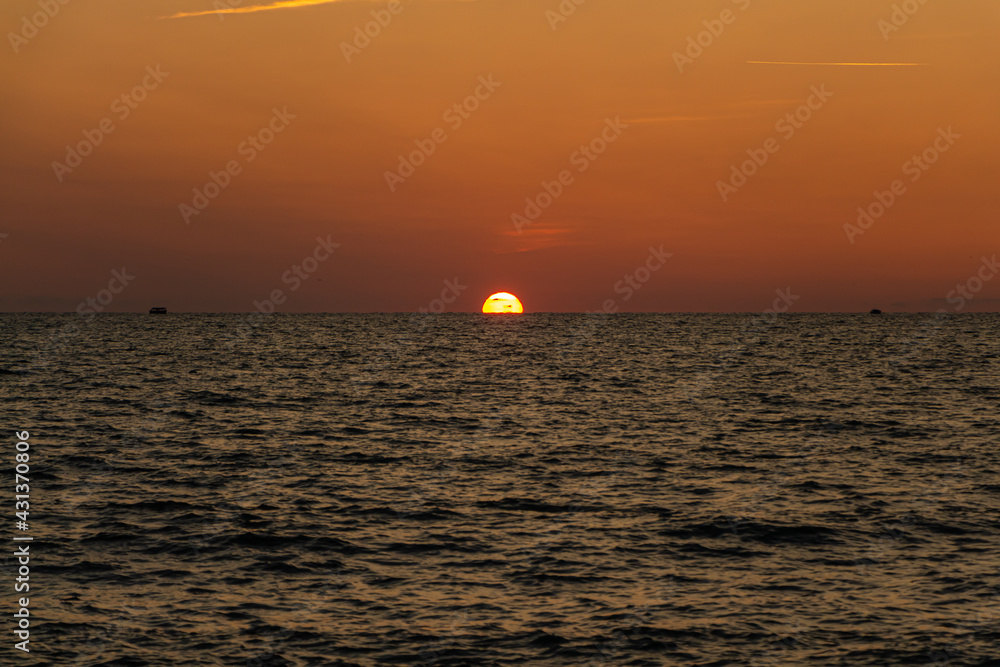 Beautiful orange sunrise is on the beach by the sea with black ship silhouettes