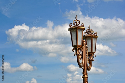 Electric street lamp exclusive shape, metal and glass, close-up against a blue cloudy sky