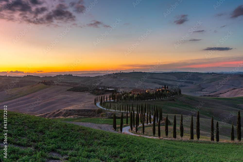 Fototapeta premium Tuscany, rural landscape at sunset. Rural farm, cypresses, green field, sunshine and clouds. Italy, Europe.