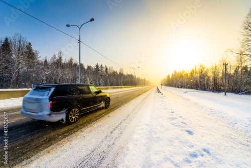 Sunrise on a clear winter morning, the car rides on the highways in the snow. View from the side of the road. Coniferous forest. Russia, Europe. Beautiful nature. © Georgii Shipin