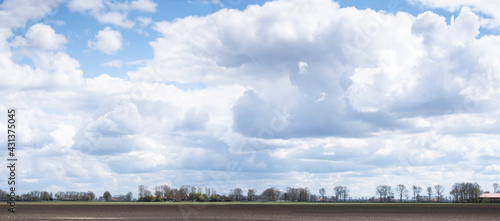 Typical Dutch flat landscape with a plowed field, a row of trees on the horizon and a blue sky with beautiful clouds in the spring. Widescreen picture