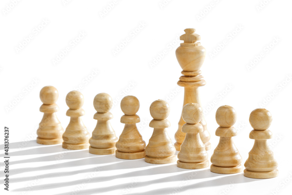 The king stands behind a row of white pawns on a white background with a long shadow. White wooden chess pieces, close-up.