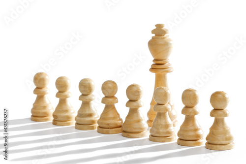 The king stands behind a row of white pawns on a white background with a long shadow. White wooden chess pieces, close-up.